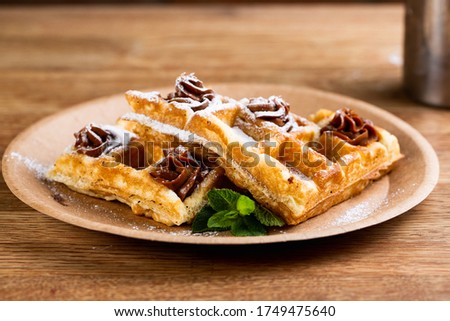Viennese waffles on a disposable plate with peanut butter, icing sugar and mint.