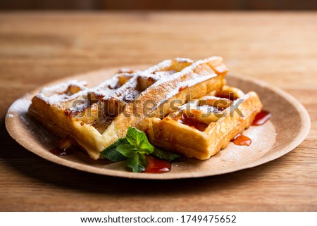 Viennese waffles on a disposable plate with strawberry jam, icing sugar and mint. cook decorates dessert with icing sugar