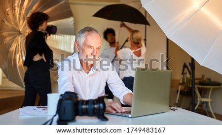 Photographer is working on pictures at laptop. Computer with team in background