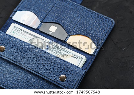 Leather Partman in blue with one hundred dollar bills and electronic credit cards on a black background.