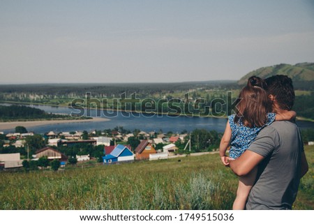 father walks with his daughter in meadow. man throws child. Village houses, forest and river as background. oncept of summer, warmth, freedom, village life, sunburn, family day