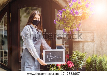 Coronavirus covid 19.Floral shop woman owner with face mask, open after lockdown quarantine. End quarantine. Announcement we are open nv doors, flower shops, coffee houses, small businesses. Sun glare