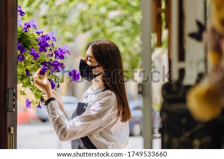 Side view close up portrait of italian woamn owner of floral shop in mask on quarantine easing, lockdown end and local business relaunch with business owner hand touching gardening flowers outdoor.