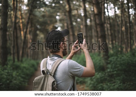 A young male tourist takes pictures on a smartphone camera in a forest. Tourism, active lifestyle