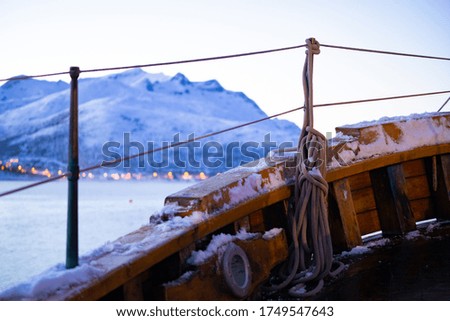 View over the front of a wooden sailing schooner. Norwegian fjord during winter in the background.