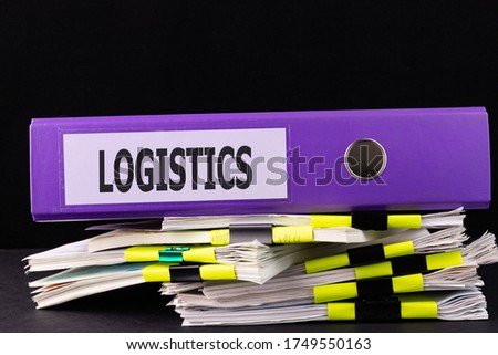 Text LOGISTICS is written on a folder lying on a stack of papers on a table. Business concept