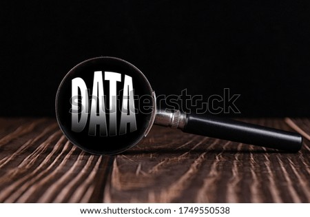 Magnifying glass with the word DATA on a wooden table and black background.