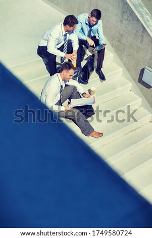 Group of handsome businessman sitting on stairs while preparing business plans during break