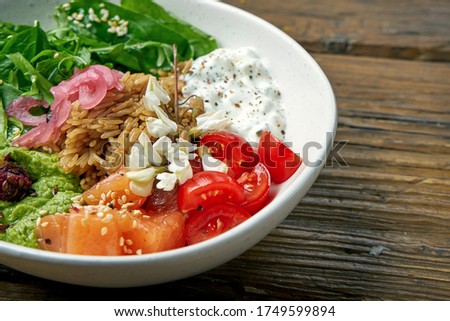 Superfood - a bowl with rice, salmon, guacamole, poached egg and cherry tomatoes seasoned with Greek yogurt on a wooden background. Balanced food