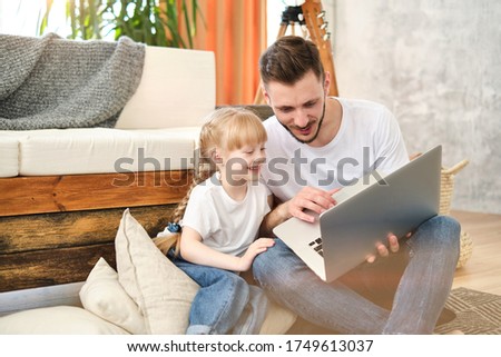 Father and daughter. Handsome young man and little cute girl lie on the carpet at home, hug, kiss, have fun. Dad and child laugh. Father's day.