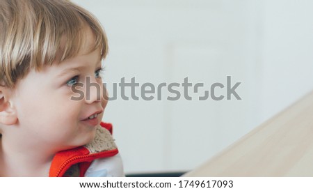 Сute little kid while watching TV. Young boy with blue eyes laughing and watch television on living room. Child watching TV, close up face of little boy, kid eyes.