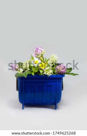 Plastic blue garbage trash bin can container with flowers, organic natural rubbish waste concept, beauty and dirty contrast at isolated background 