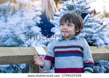 Portrait cute little boy looking up with blurry christmas tree background, Kid playing outdoor in winter fair, Child having fun with snow foam at Christmas market.