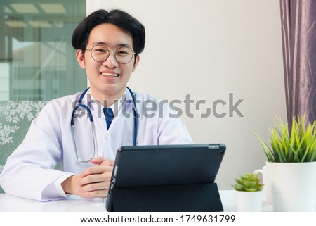 Happy Asian young doctor handsome man smile wear glasses use modern smart digital tablet computer sit and listen patient explain symptoms on desk at hospital office, Technology Healthcare And Medicine