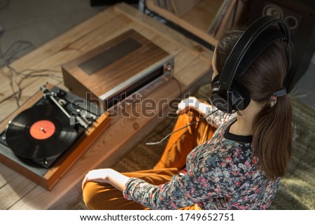 Young Woman listening a music on a HiFi system with turntable, amplifier, headphones and lp vinyl records in a listening room Royalty-Free Stock Photo #1749652751