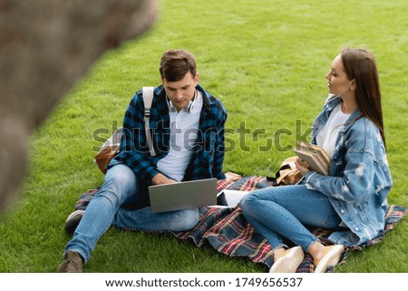 selective focus of cheerful girl holding books and looking at handsome student using laptop, online study concept