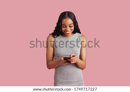 Studio portrait of a smiling young woman entrepreneur in business dress, writing or texting using her phone