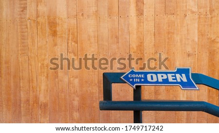 Text on vintage sign "Come in open" invites customers into a store. on rustic wooden wall.