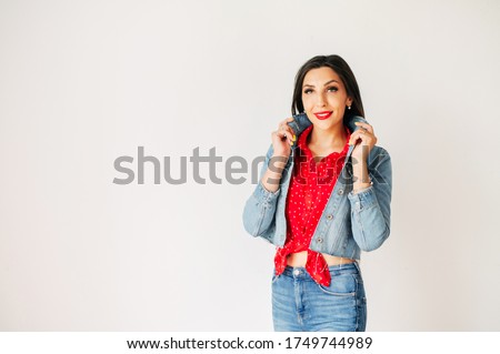 Lovely young brunette woman in jeans suit and red shirt posing on white background