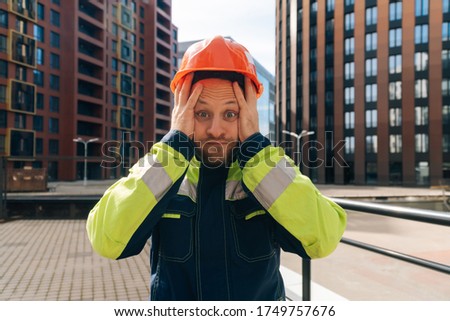 a clean builder shows sincere emotions of indignation. Man in special clothes and helmet shows hostility against the background of a ready-made business center