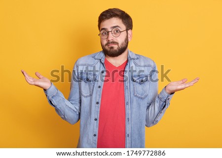 Image of magnetic handsome helpless young man shrugging with shoulders, looking directly at camera, raising arms, having confused facial expression, wearing casual clothes. Emotions concept. Royalty-Free Stock Photo #1749772886