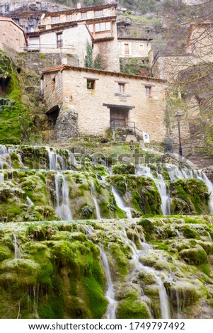Village of Orbaneja del Castillo in the upper part of the image, in the foreground the main waterfall runs over the rocks and green moss. Long exposure. Castilla León, Spain