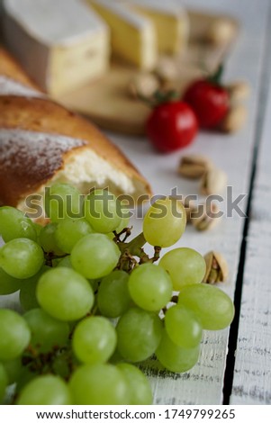 Delicious tasty french cuisine appetizer kit: green grapes, baguette, pistachios, cheese, tomatoes. French snacks and a glass of white wine. Black olives. White wooden table and background. Top view