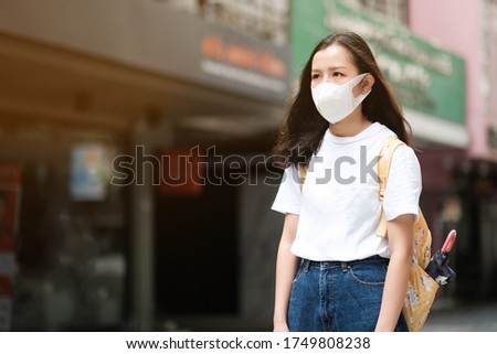 Asian girl in white t-shirt with yellow bag wear surgical mask to protect the Covid-19 virus in public areas, New normal lifestyle 