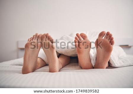 Close up photo of four legs in bed belonging to loving couple