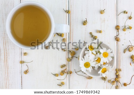 Herbal tea with fresh chamomile flowers in a ceramic mug on white wooden background