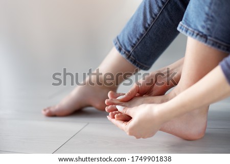 Tired woman doing self foot massage for pain relief after fatigue, long walking, working, standing, flat feet or injury, sitting indoors. Suffering from hurt of arch, ball, heel or toe treatment Royalty-Free Stock Photo #1749901838