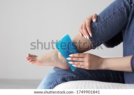 Close up woman feet and legs, and hands holding ice gel pack as cold compress on ankle due to stretching or injury, sitting on bed in apartment indoors Royalty-Free Stock Photo #1749901841