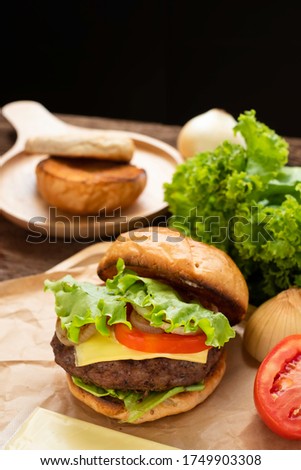 Homemade cheese beef burger with ingredient like tamoto & onion on wood background. Beef hamburger stuff with grill cheese in crispy hamburger bun. Homemade cheese beef burger & junk food concept. 