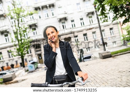 An attractive smiling girl talks on phone, street background. Cute girl stopped on the bicycle to talk on the phone, she smiles wearing casual clothes