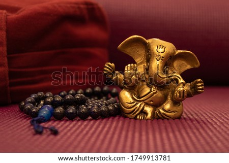 Golden sculpture of ganesha on a yoga mat and blue prayer beads next to yoga pillow. Meditation and yoga concept.