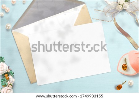 Blank post card, craft paper envelope and wedding decoration environment objects on blue background. Wedding workspace concept scene.
