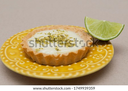 Side view of lemon tart on dish plate with lemon slices on table. Lemon tartlet with zest on top. Strawberry Pastry. Sweet with citrus fruit. Selective focus. Copy space.