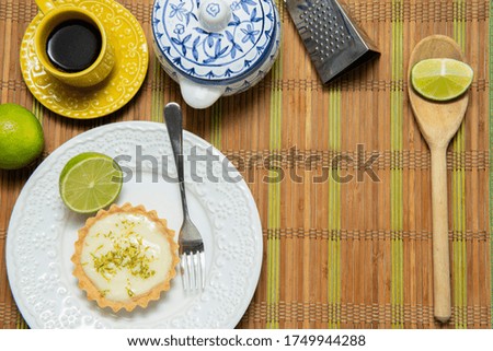 Top view of frame of various kitchen accessories. Yellow coffee cup, lemon tart on blue plate, spoon, cutting board, stainless steel spatula, grater with blank space for text. Copy space.