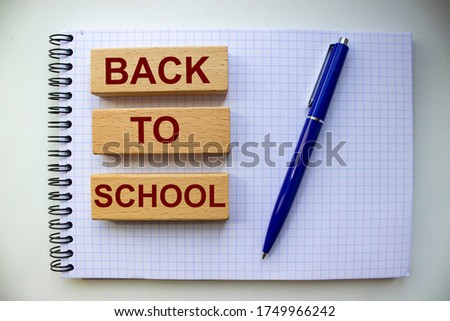 The inscription back to school on wooden blocks on a notepad with a blue ballpoint pen.