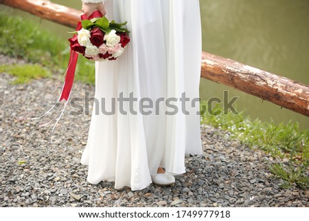 The bride walks along a lake with water and a tree with a bouquet of flowers.
