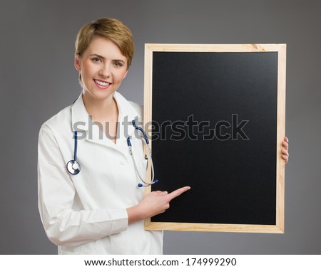 Smiling female nurse holding black board. Waist up studio shot on gray background.