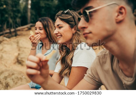 Young people eating potato chips in the field near a lake in nature in summer.