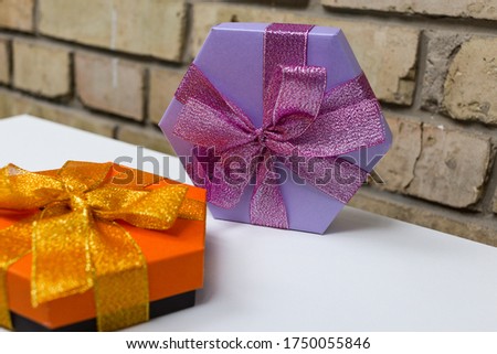 A beautiful orange and lilac hexagon gift boxes with ribbon and bow on the white table and brick background. Flat lay. Place for text. Present