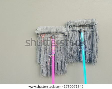 two mops the right handle is green pink left handle leaning on a smooth cement surface