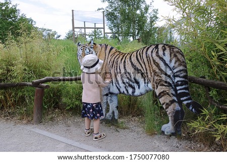 A little girl in the zoo is touching paper tiger 