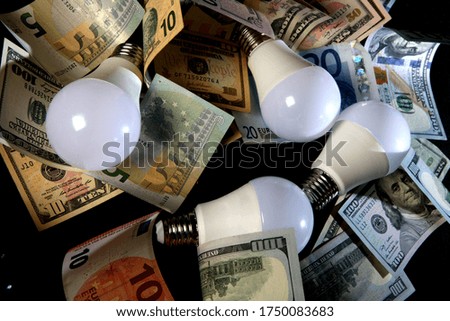 several modern energy-saving light bulbs on the background of many banknotes