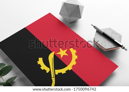 Angola flag on minimalist paper background. National invitation letter with stylish pen on stone. Communication concept.