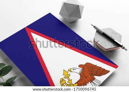 American Samoa flag on minimalist paper background. National invitation letter with stylish pen on stone. Communication concept.