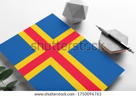 Aland Islands flag on minimalist paper background. National invitation letter with stylish pen on stone. Communication concept.