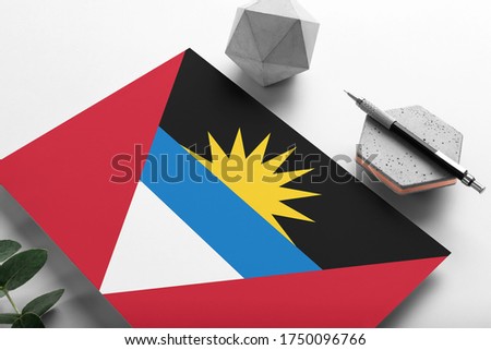 Antigua and Barbuda flag on minimalist paper background. National invitation letter with stylish pen on stone. Communication concept.